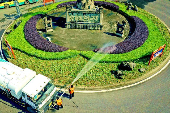 近日,万东北路龙凤碑转盘,园林工人正在为交通绿岛内的植被浇水.